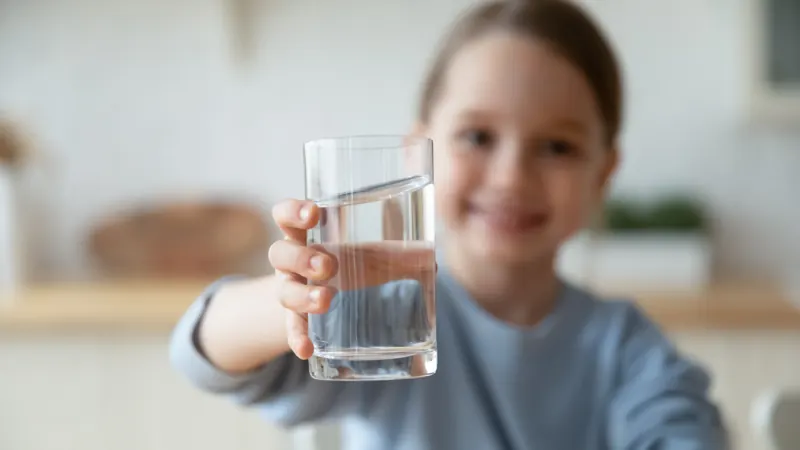 Una bambina sorridente porge un bicchiere d'acqua
